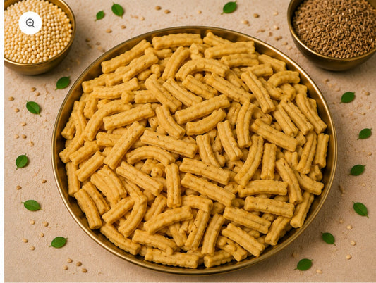 Crispy golden snack sticks in a brass bowl surrounded by seeds and curry leaves.
